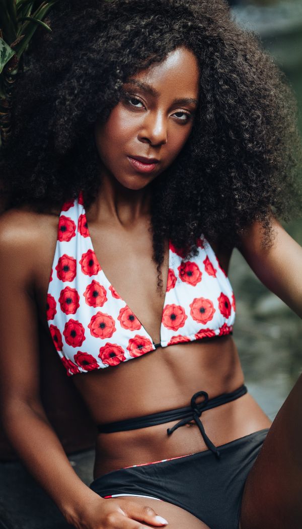 Woman wearing a red and white poppy flowers bikini top with black bottoms.
