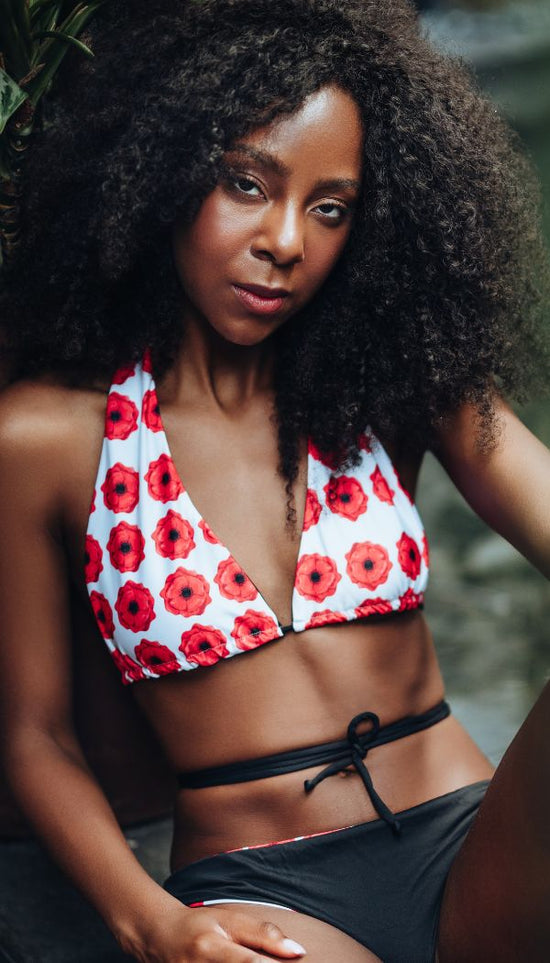 Woman wearing a red and white poppy flowers bikini top with black bottoms.